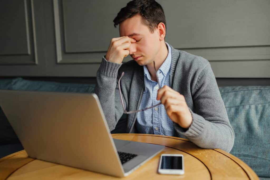 Feeling fatigued. Frustrated young man massaging his nose and keeping eyes closed while working in cafe.