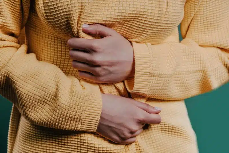 Person wearing a yellow textured top holds their stomach with both hands, suggesting possible discomfort or pain—perhaps seeking the best SIBO treatment in Maine for relief. in Portland Maine
