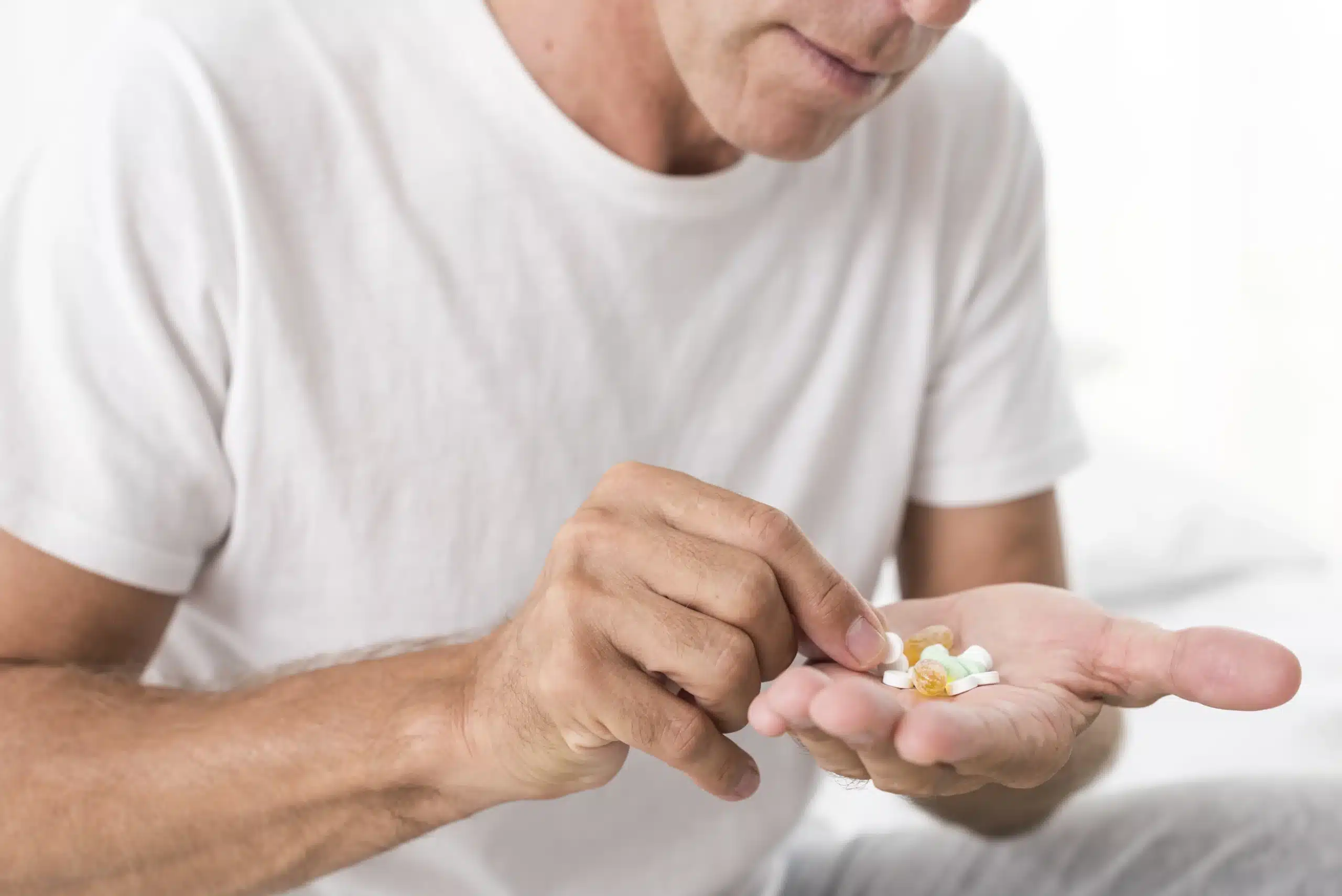 A man in a white shirt holds various pills in one hand and selects one with the other hand, illustrating male nutrition guidance as part of effective men’s wellness strategies. in Portland Maine