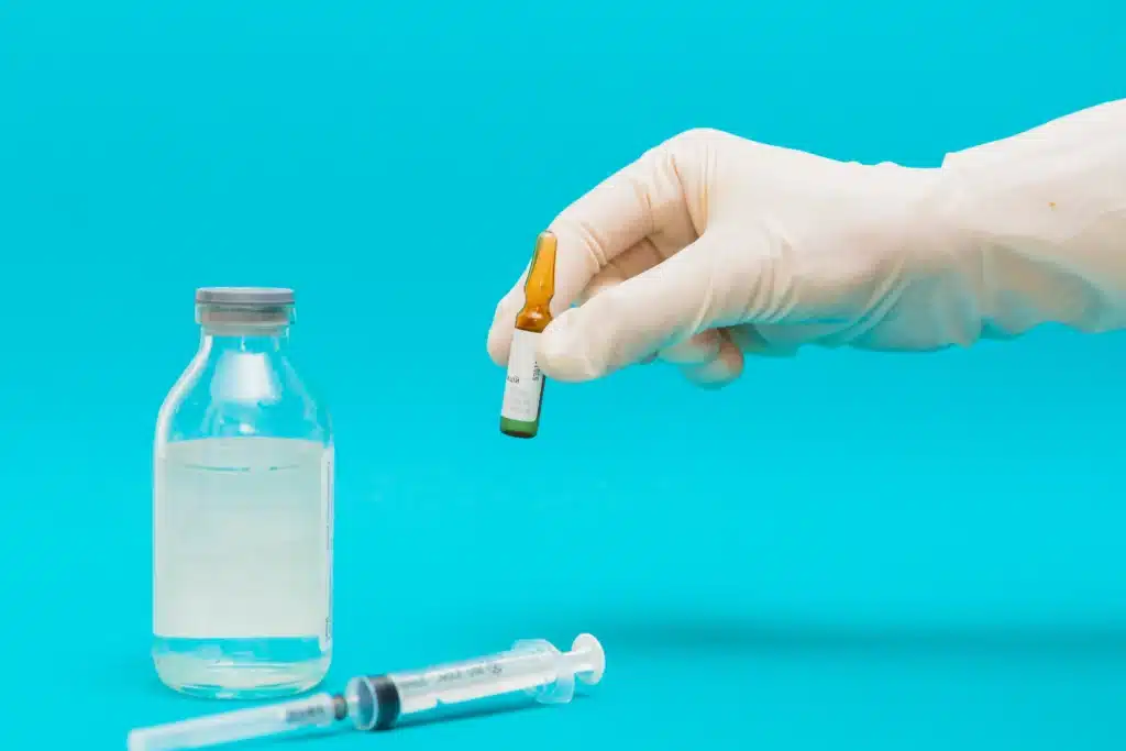 A gloved hand holds a small vial next to a larger vial of liquid and a syringe, illustrating a GLP-1 medication comparison against a blue background. in Portland Maine
