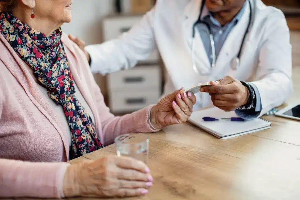 A doctor hands medication for Female Hormone Replacement to an older woman holding a glass of water; a clipboard and pen are on the table. in Portland Maine
